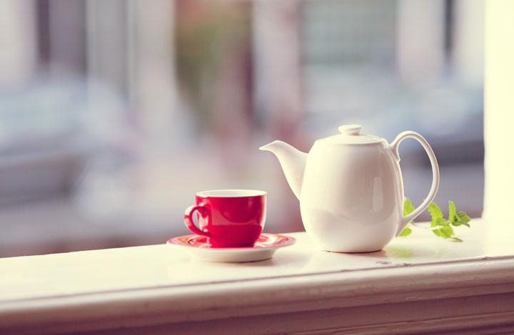A teapot and cup sitting on a window ledge 