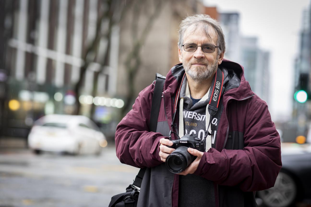 An older man holding a camera on a city street