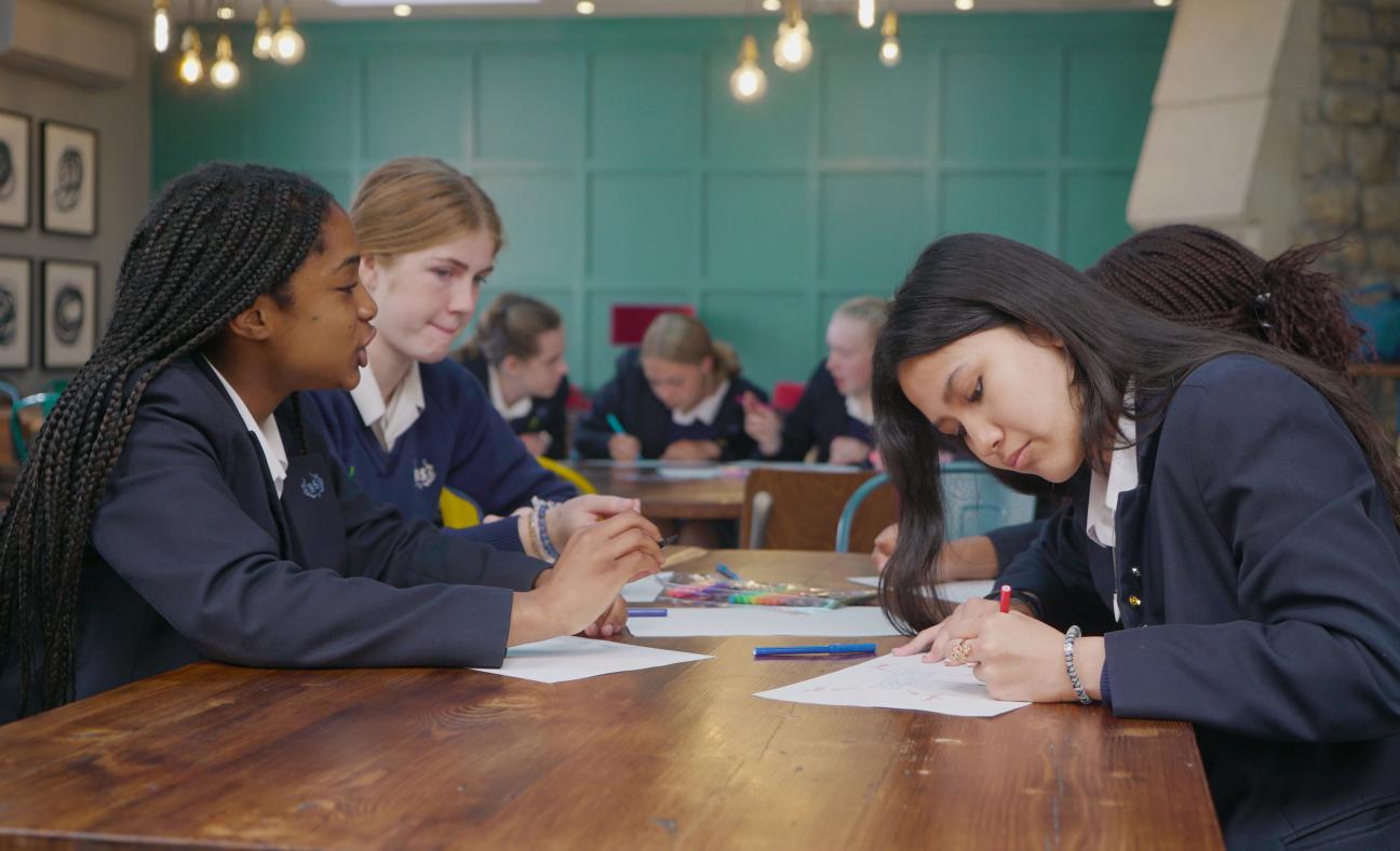 3 school pupils sat around a table, working on peer education mental health resources