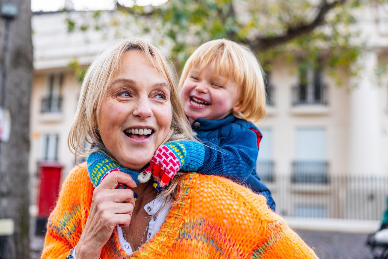 A smiling woman carries a child on her back