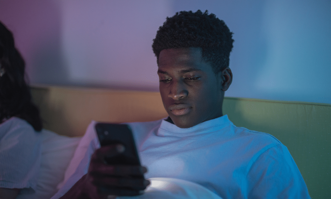 Young Black man reading his phone while sat on a sofa