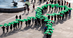 People holding green umbrellas to make the shape of a mental health awareness ribbon