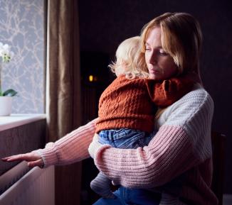 A woman holding a baby feels for heat from a radiator