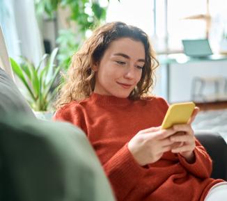 A woman sits on the sofa looking at her phone and smiling