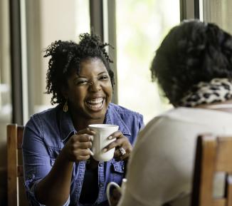 Two friends laugh and drink coffee
