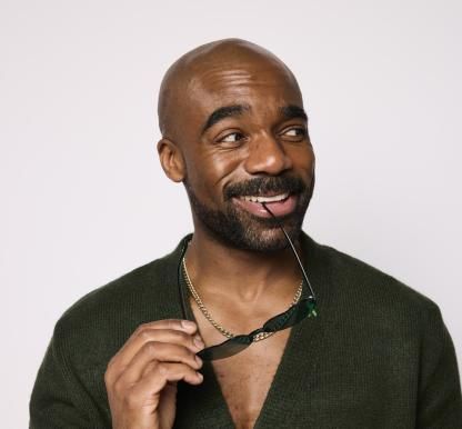 Ore Oduba holding green sunglasses and wearing a green cardigan