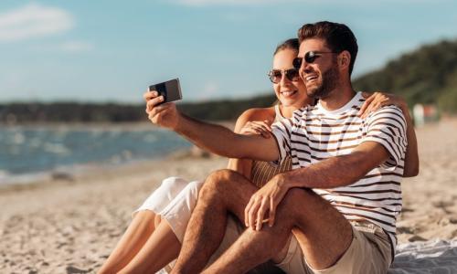 Two people sitting on a beach taking a selfie