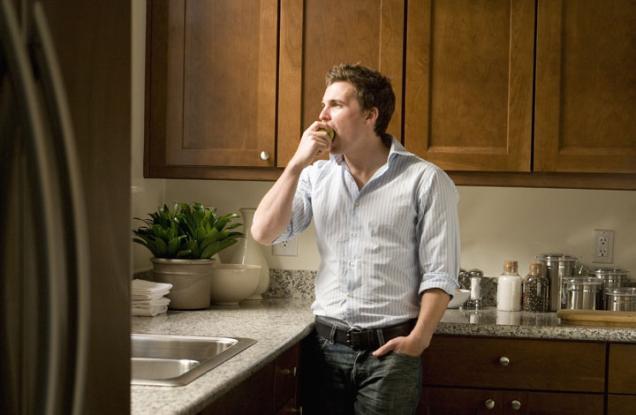 Young man in a kitchen eating an apple