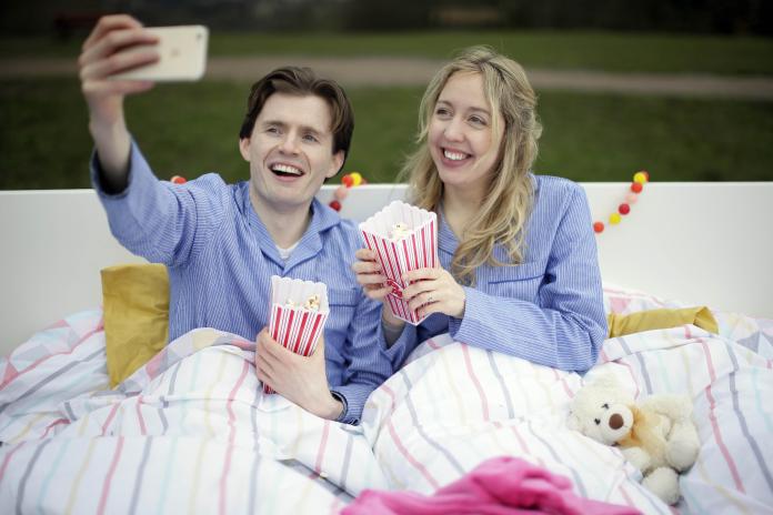 Image of a couple in bed, taking a selfie together on a smart phone