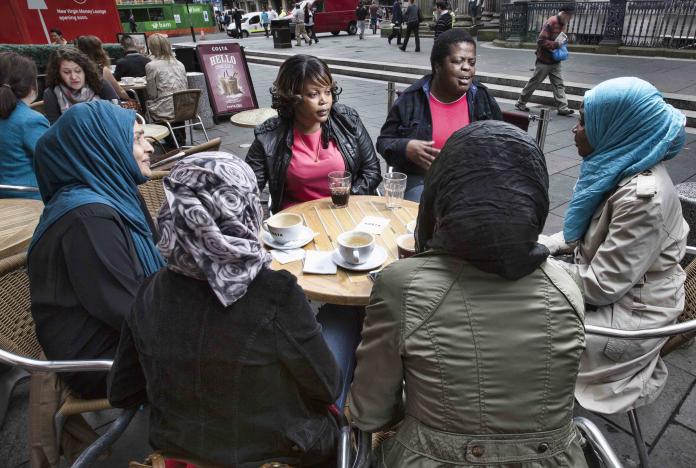 A group of BAME women sitting outside, talking and drinking coffee