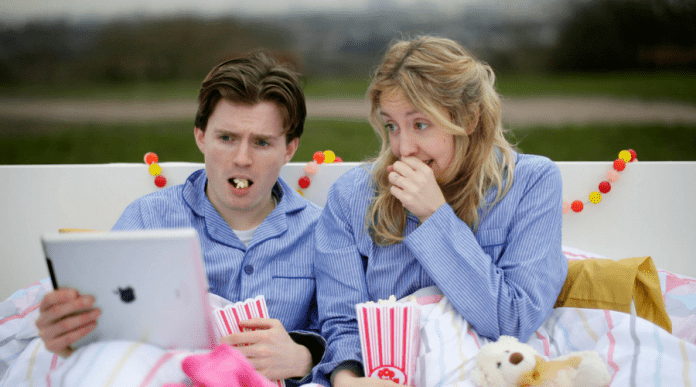 Foto de una pareja en la cama comiendo palomitas de maíz y viendo algo en una computadora portátil