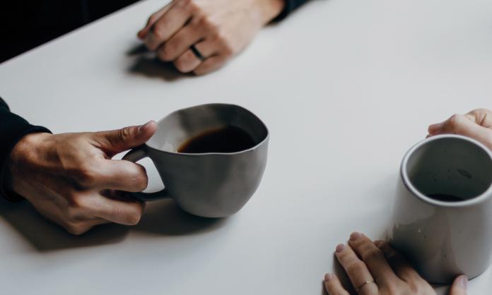 A close up of two hands holding cups of coffee over a white table