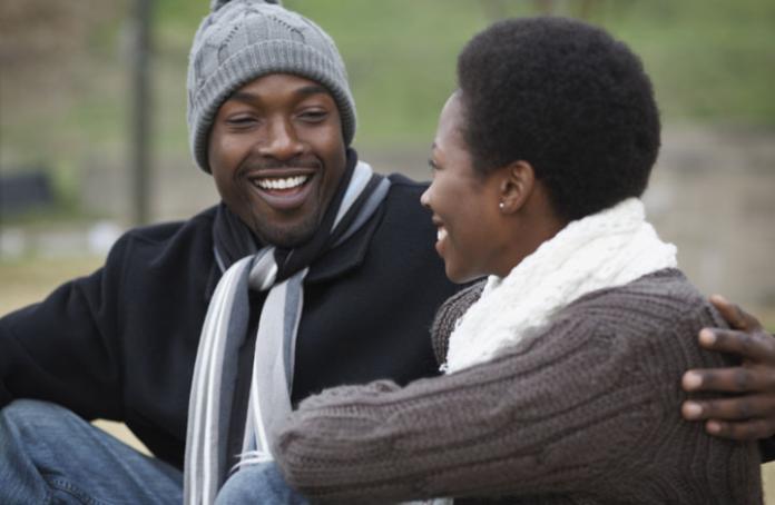 Black man with arm around black lady, both smiling