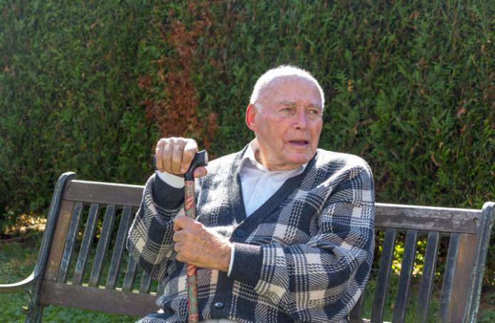 Elderly man sat on a bench with his cane