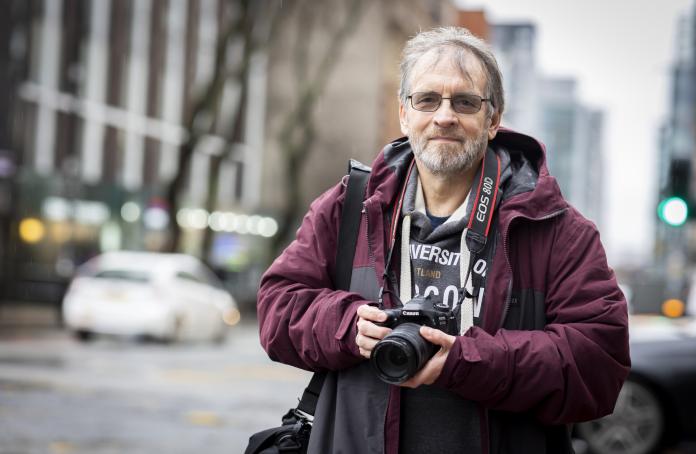 An older man holding a camera on a city street