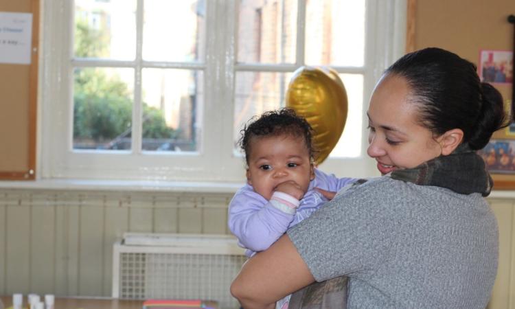 Photo of a mother holding her baby, with arts and crafts activities in the background