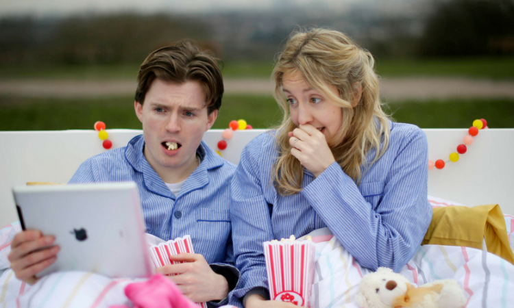 Photo of a couple in bed eating popcorn and watching something on a laptop