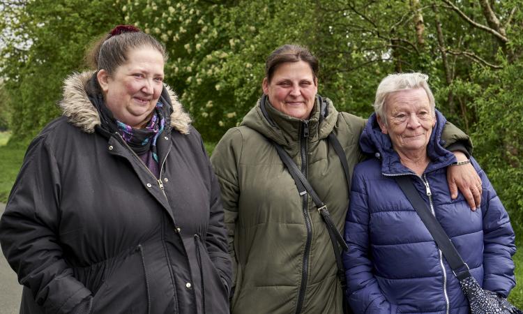 A group of three women standing in front of some tree