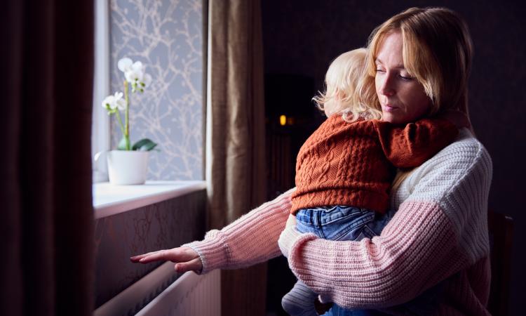 A woman holding a baby feels for heat from a radiator