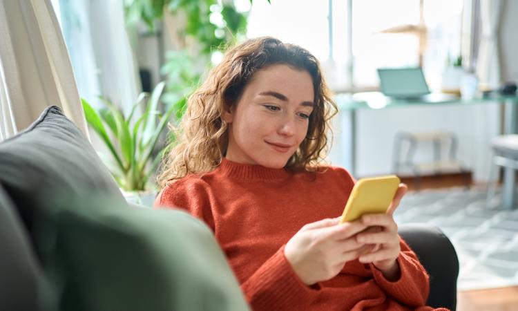 A woman sits on the sofa looking at her phone and smiling