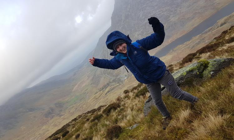 A woman stands with her arms in the air on a windy hillside.