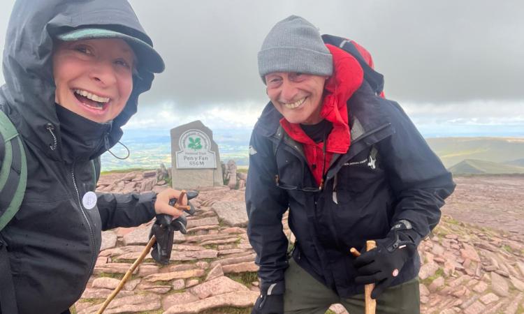 A couple stood smiling in the wind at the top of Pen Y Fan mountain