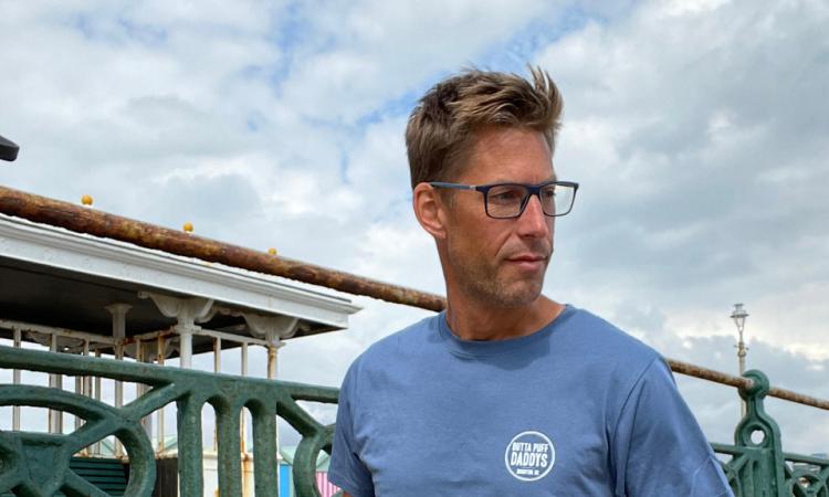 Paul Jukes walking on a beach wearing blue Outta Puff Daddys t-shirt and jeans
