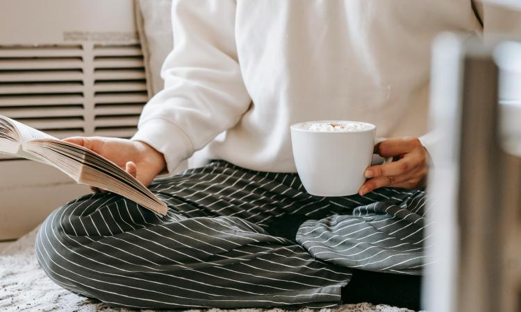 A person sitting on the floor with a cup of coffee and a book