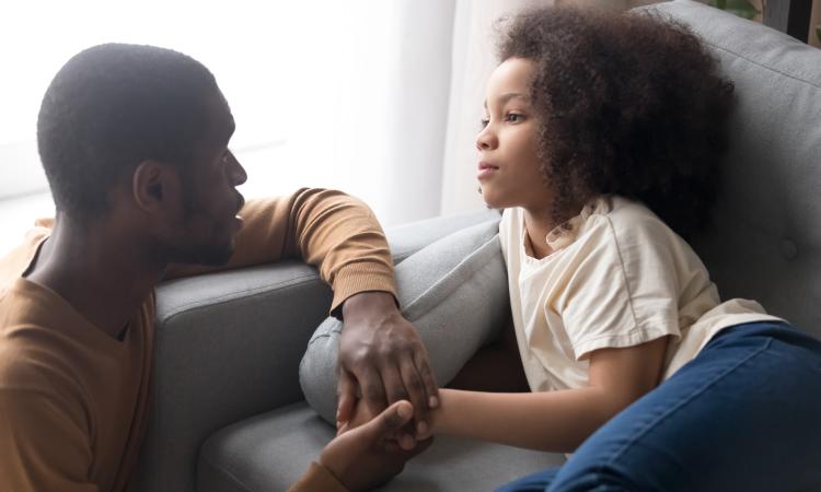 A father and daughter talking as she lies on a sofa