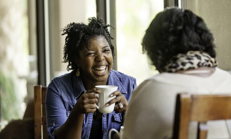 Two friends laugh and drink coffee