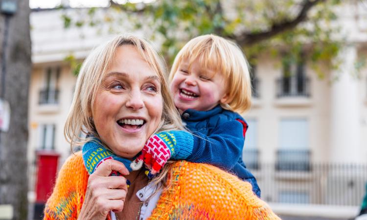 A smiling woman carries a child on her back