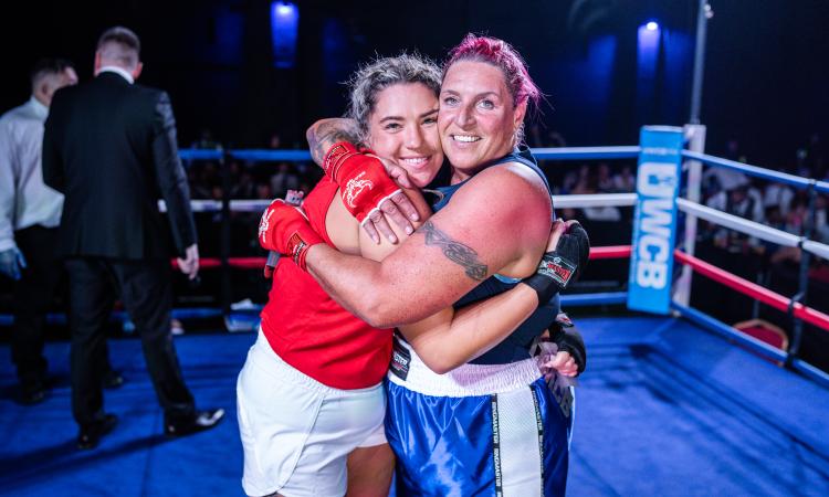 Two female boxers embracing in the centre of the ring.