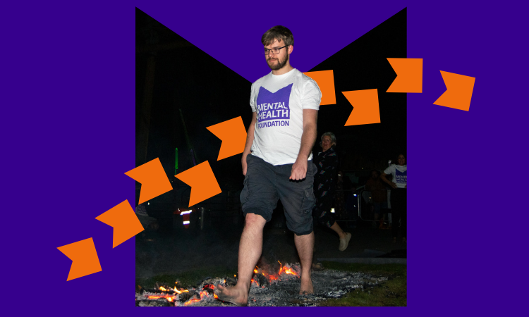 A man wearing an MHF t-shirt walking over hot coals at night