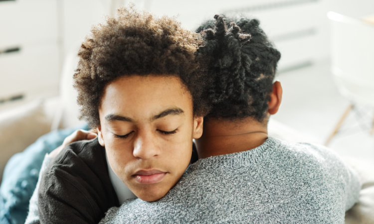 A young man hugs a person with his eyes shut. 