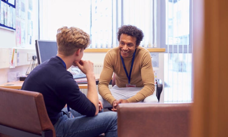 A young man talking to a mentor both sat across a desk