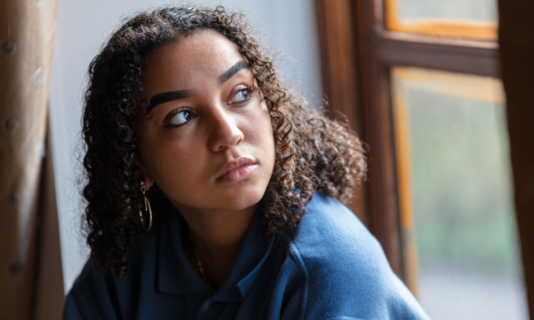A young Brown woman sat looking out of a window. 