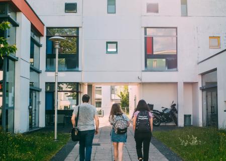 Image of three students seen from the back as they walk across ta university campus with white buildings