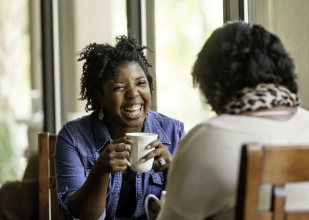 Two friends laugh and drink coffee