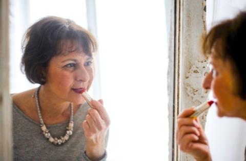 Older woman applying lipstick in the mirror