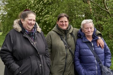 A group of three women standing in front of some tree