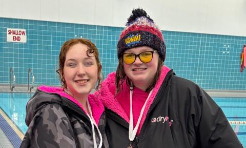 Two young people wearing dry robes next to a swimming people