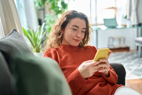 A woman sits on the sofa looking at her phone and smiling