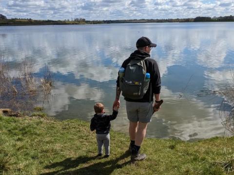 A man holds a child's hand as they look onto a body of water