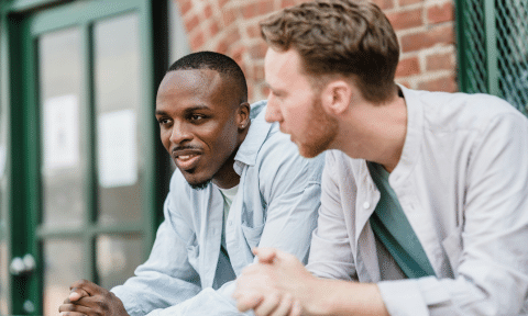 Two men stood leaning on a fence side by side in conversation