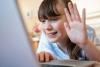 Photo of a child on a video call, waving at their laptop